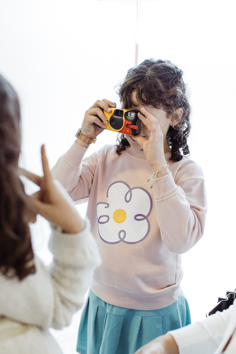 Criança fotografando com uma câmera analógica amarela durante a festa